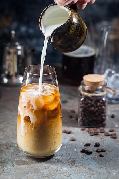 Ijskoffie koude zomerdrank in een hoog glas met gietroom en koffiebonen op een stenen achtergrond.