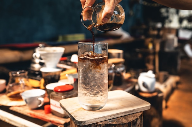 IJskoffie maken, handen schenken koffie in een glas koud water.