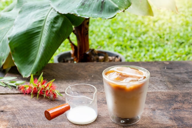 Ijskoffie met melk op houten tafel tegen bananenbladeren.