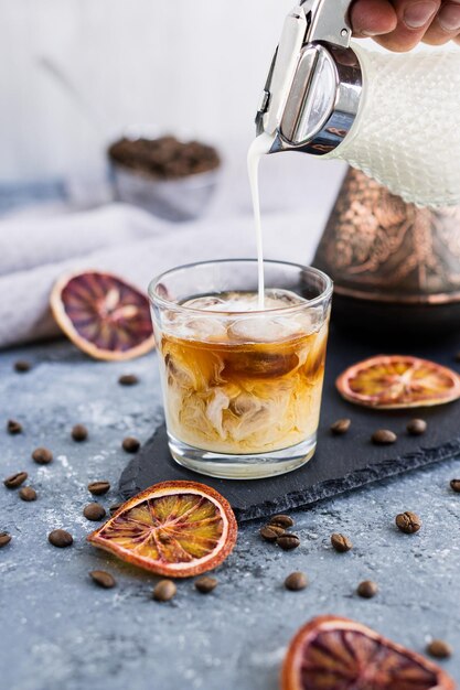 IJskoffie met melk Zomerdrankje Gietende melk in koffie met ijsblokje op grijze achtergrond