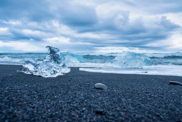 Foto ijsschotsen op een zwart zandstrand met golven die naar de kust rennen tegen de lucht