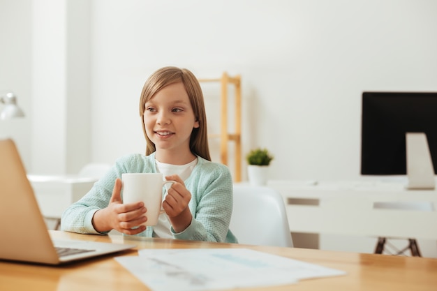 IJverig briljant mooi meisje aan de tafel zitten en iets op haar computer te lezen