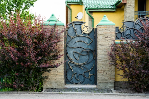 Foto ijzeren toegangspoort met smeedelementen met een stenen hek die het huis versieren