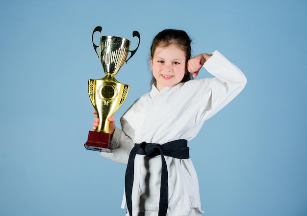 Ik ben de beste knock-out energie en activiteit voor kinderen die Kung Fu beoefenen, gelukkig jeugdsportsucces in een tweegevecht meisje met kampioensbeker vechtsportwinnaar klein meisje in gi sportkleding