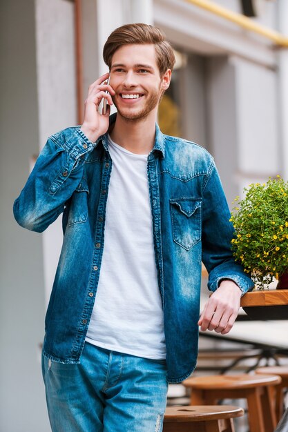 Ik ben er al! Vrolijke jonge man praten op de mobiele telefoon en glimlachend in de camera