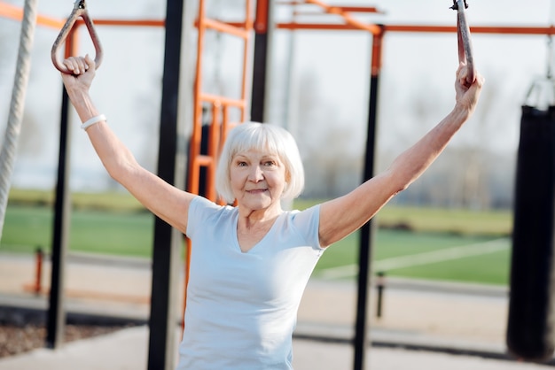 Ik ben geïnspireerd. Blije blonde vrouw die kin-ups doet tijdens het sporten in de open lucht