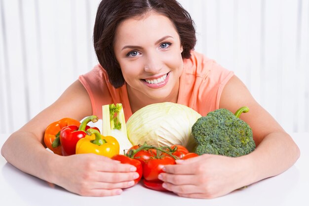 Ik ben vegetariër. Mooie jonge vrouw die verse groenten knuffelt die op tafel ligt en glimlacht