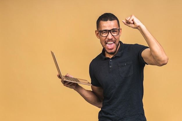 Ik ben winnaar opgewonden gelukkige afro-amerikaanse zwarte man met laptopcomputer en het vieren van de overwinning geïsoleerd op beige achtergrond