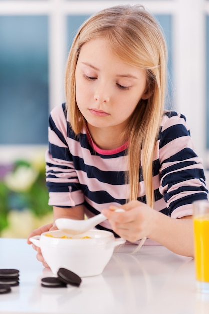 Ik heb geen honger. Verdrietig meisje eet iets van het bord terwijl ze aan tafel zit