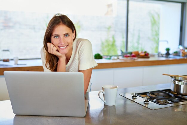 Ik heb honderden menu-ideeën gevonden Portret van een aantrekkelijke jonge vrouw die haar laptop in de keuken gebruikt