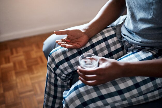 Ik heb medicijnen nodig om van deze griep af te komen Bijgesneden opname van een onherkenbare man die alleen op zijn bed zit en pijnstillers neemt met water