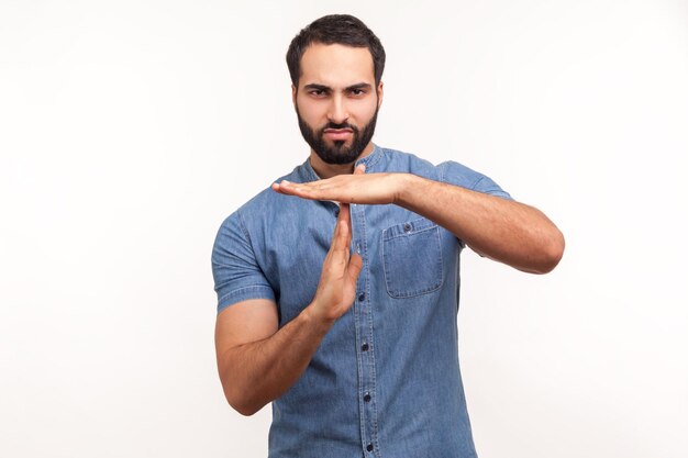 Ik heb meer tijd nodig. Moe bebaarde man in blauw shirt met time-out gebaar, problemen hebben en pauze of meer tijd nodig hebben, professionele burn-out. Indoor studio-opname geïsoleerd op een witte achtergrond