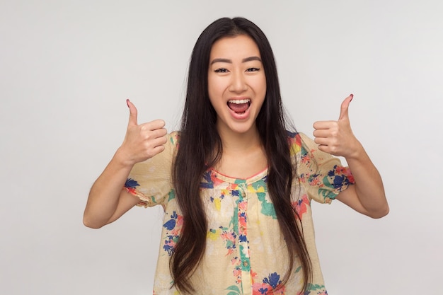 Ik hou ervan Opgetogen mooi meisje met donkerbruin haar in zomerblouse schreeuwend van opwinding en duimen opdagen als gebaar emotionele reactie op uitstekende service binnen studio-opname geïsoleerd