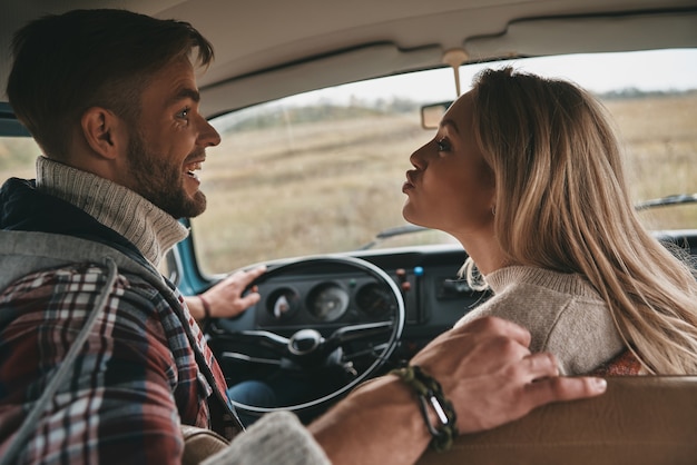 Ik hou van alles aan haar. Speelse jonge vrouw die een gezicht trekt terwijl ze op de passagiersstoel voorin zit in een minibusje in retrostijl met haar vriendje