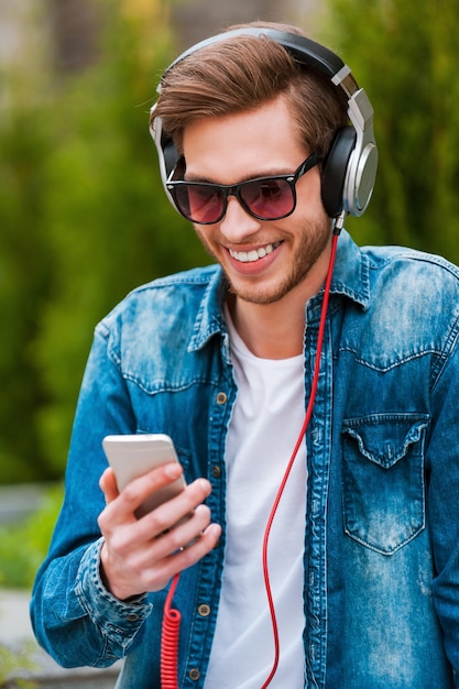 Ik hou van dit liedje! Gelukkige jonge man in koptelefoon met mobiele telefoon en glimlachend