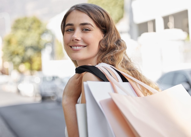Ik hou van een beetje winkelen in de middag Bijgesneden portret van een aantrekkelijke jonge vrouw die door de stad loopt met haar boodschappentassen in de hand