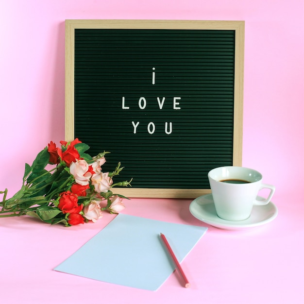 Ik hou van je op letterbord met kopje koffie, rozen en potlood op blanco papier geïsoleerd op roze achtergrond