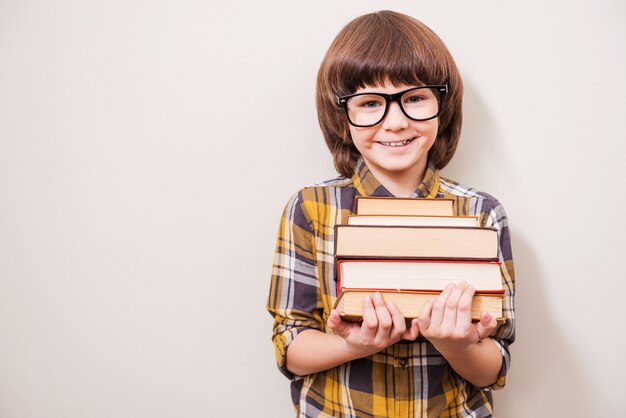 Ik hou van lezen! Fijne kleine jongen die een boekstapel vasthoudt en glimlacht terwijl hij tegen een grijze achtergrond staat