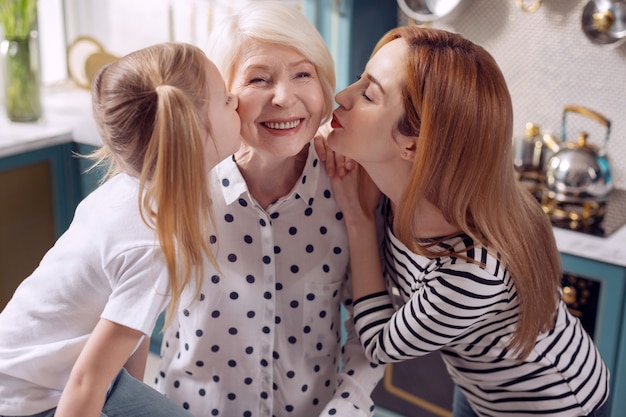 Ik hou van onze oma. Leuk meisje en haar moeder die een hogere vrouw samen op de wangen kussen terwijl de vrouw gelukkig glimlacht