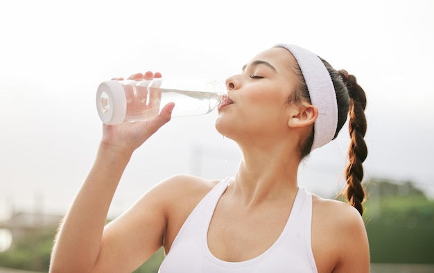 Ik kan er gewoon geen genoeg van krijgen. shot van een mooie jonge vrouw die een fles water drinkt terwijl ze aan het tennissen is.