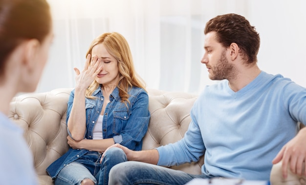 Ik kan mijn gevoelens niet binnen houden. Triest depressieve blonde vrouw zittend in het kantoor van de psycholoog en haar gezicht te sluiten tijdens het huilen