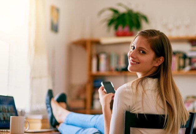 Ik kan mijn leven zonder wifi niet voorstellen Portret van een jonge vrouw die haar smartphone gebruikt terwijl ze thuis aan haar bureau zit