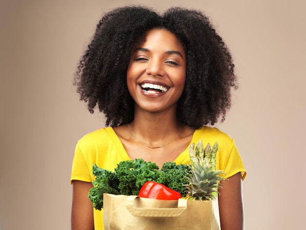 Ik kan niet wachten om aan mijn nieuwe dieet te beginnen Studio-opname van een aantrekkelijke jonge vrouw met een zak vol groenten tegen een bruine achtergrond