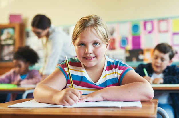 Ik krijg al mijn antwoorden goed Shot van een jong meisje dat in haar klas op school zit en in haar werkboek schrijft