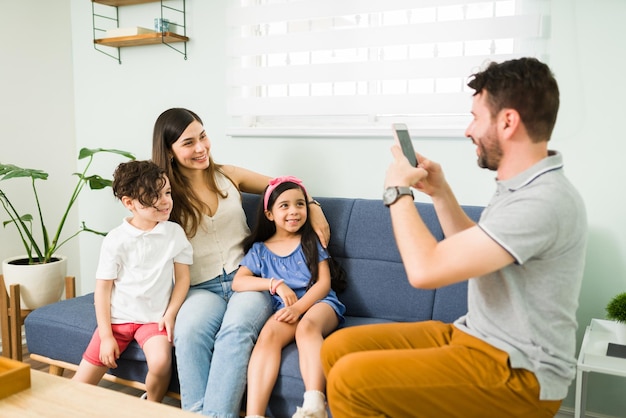 Ik plaats deze foto op sociale media. liefdevolle spaanse man die een foto maakt met een smartphone voor haar vrouw en schattige kinderen