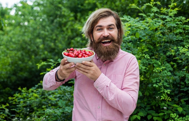 Ik vind het lekker biologisch fruit zelfverzekerde boer met vers fruit bebaarde man met rijpe kersen Oogsten in de zomer gelukkige volwassen hipster met baard brutale blanke man met kers