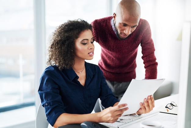 Ik was net dit papierwerk aan het lezen. Bijgesneden opname van een mannelijke supervisor die een aantrekkelijke jonge zakenvrouw helpt terwijl ze op kantoor werkt