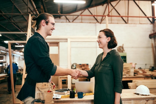 Foto ik werk alleen met de beste bijgesneden opname van twee jonge timmerlieden die elkaar de hand schudden terwijl ze samenwerken in hun werkplaats