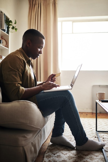 Ik werk te hard om mezelf niet te verwennen Volledig shot van een knappe jonge man die een laptop en een creditcard gebruikt om online te winkelen terwijl hij thuis op zijn bank zit