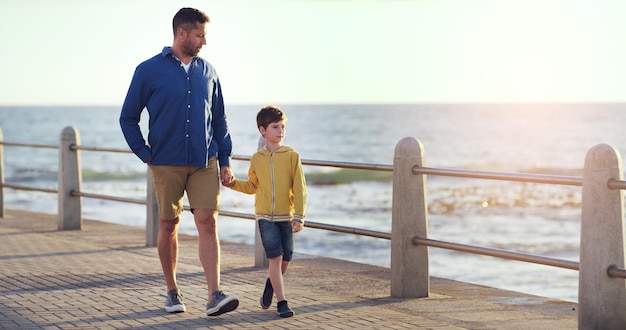 Ik zal er altijd zijn om zijn hand vast te houden Shot van een vader en zoon die elkaars hand vasthouden terwijl ze op een loopbrug bij het strand lopen