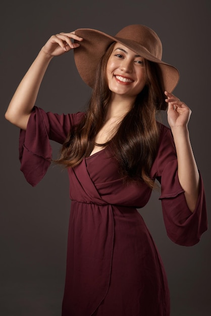 Ik zou niet gelukkiger kunnen zijn met mijn hoed Bijgesneden portret van een aantrekkelijke jonge vrouw die in de studio poseert tegen een grijze achtergrond