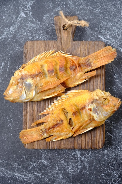 Ikan nila goreng. fried tilapia served on wooden teak cutting board. animal protein. Indonesian food