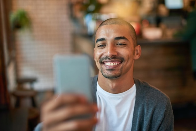 カフェであなたを待っていますカフェで彼の携帯電話にテキストメッセージを送る若い男のトリミングされたショット