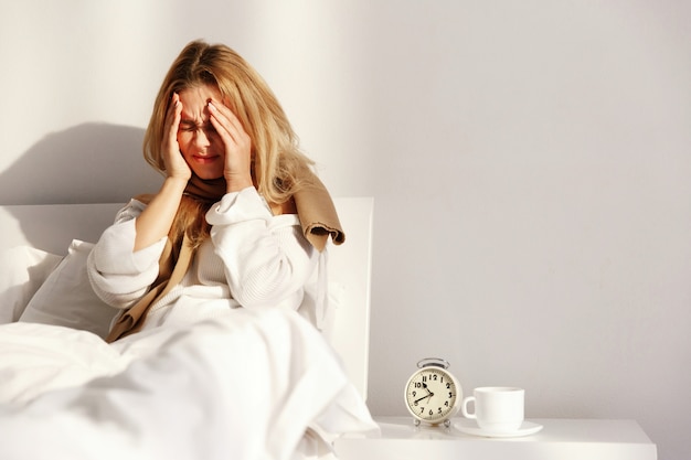 Photo ill blonde woman lies with a scarf in the bed with headache and fever