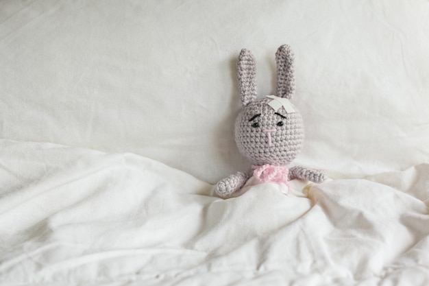 Ill Grey toy rabbit with plaster on head in white bedroom.