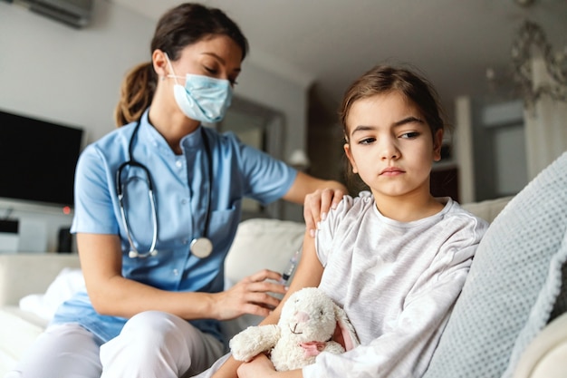 Bambina malata che si siede sul divano a casa e riceve l'iniezione durante l'epidemia di covid