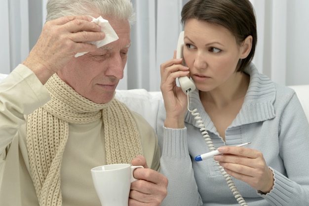 Ill Senior man and caring daughter with thermometer calling