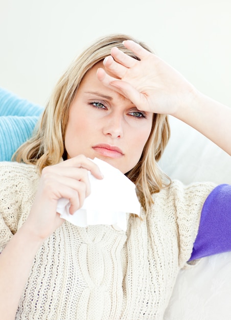 Ill woman holding a tissue sitting on a sofa