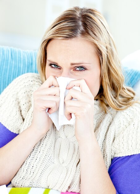 Ill woman using a tissue sitting on a sofa