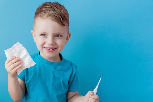 Ill young child with a thermomether measuring the height of his fever and looking into the camera