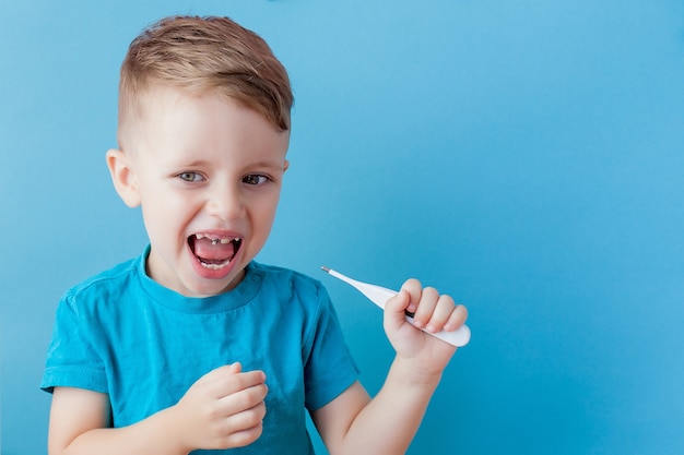 Ill young child with a thermomether, measuring the height of his fever and looking into the camera.