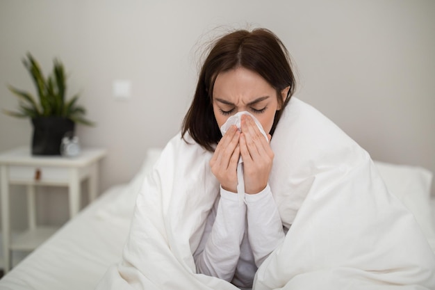 Ill young lady sneezing staying in bed at home