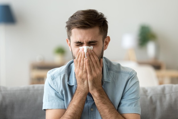 ill young man sneezing in handkerchief blowing wiping running nose