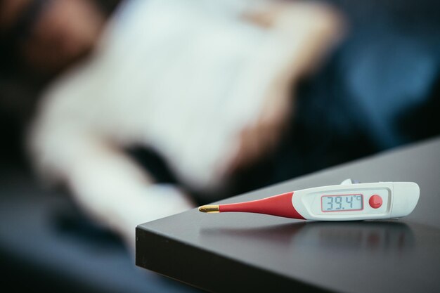 Photo illness and fever thermometer and ill man lying on the sofa in the blurry background