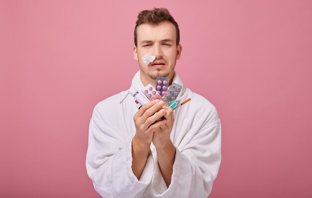 Illness man with temperature in white coat with an enemin one hand and pills and syringe in second