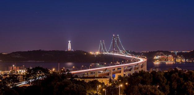 Illuminated 25 de abril bridge over tagus river by christ the king against sky at night
